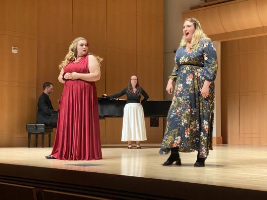 three singers on stage with a piano accompanist